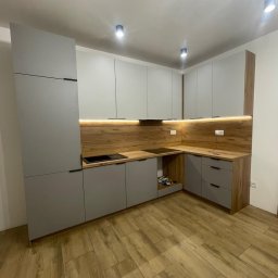Szara kuchnia na wymiar z drewnianym blatem i oświetleniem LED w Będzinie. Nowoczesny design, minimalistyczne uchwyty, płyta indukcyjna. Widok na całą zabudowę kuchenną.
