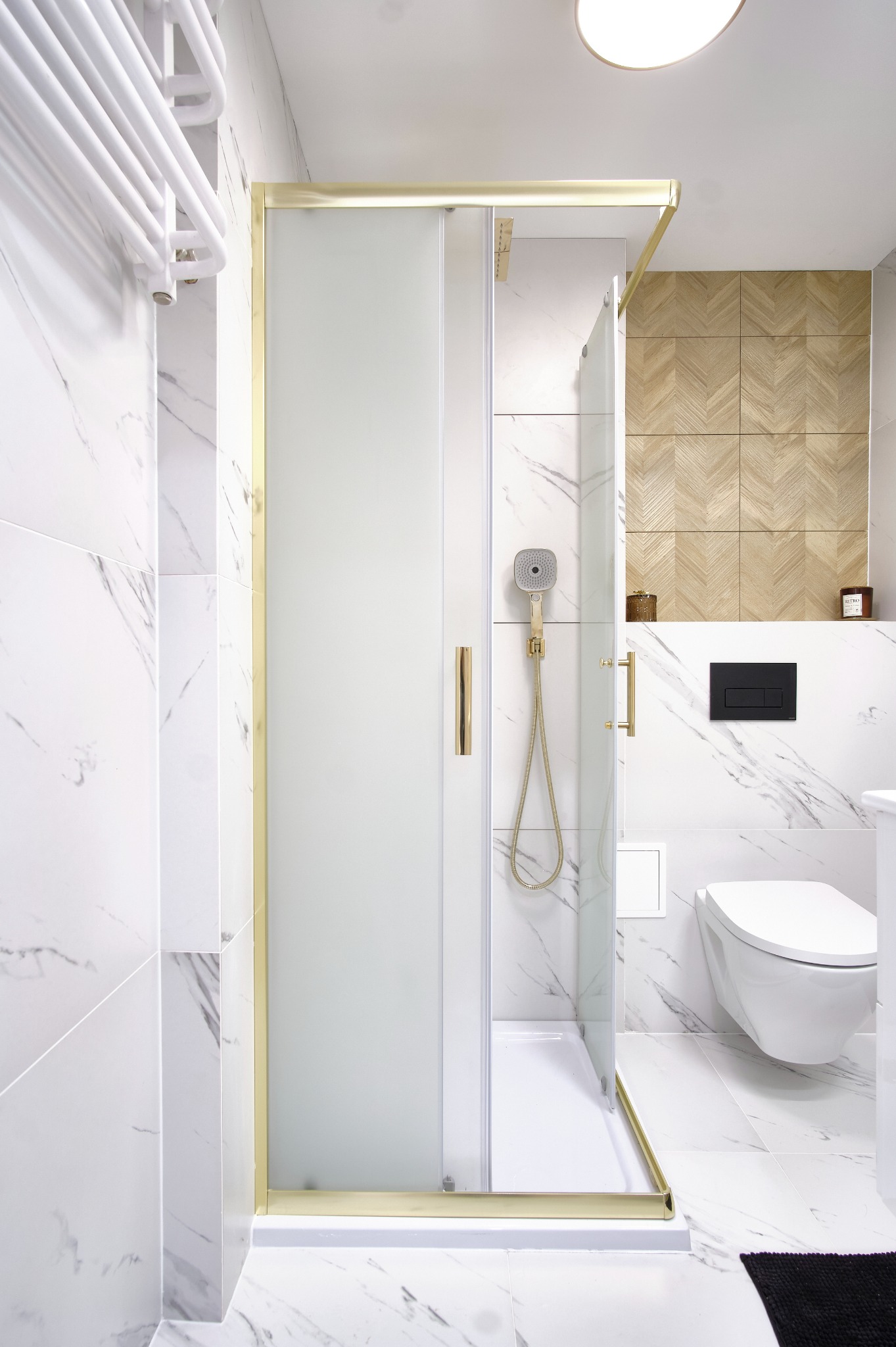 Nowoczesna łazienka z kabiną prysznicową w złotej ramie, białe marmurowe płytki i drewniane akcenty. Minimalistyczny design, wisząca toaleta.