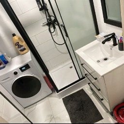 CLEAN INTERIOR 24 TOMASZ KASZUBOWSKI - Wnętrze łazienki z pralką, kabiną prysznicową i umywalką. Na pralce stoją środki czystości. Widok z perspektywy drzwi, z lekkim obrotem kadru.