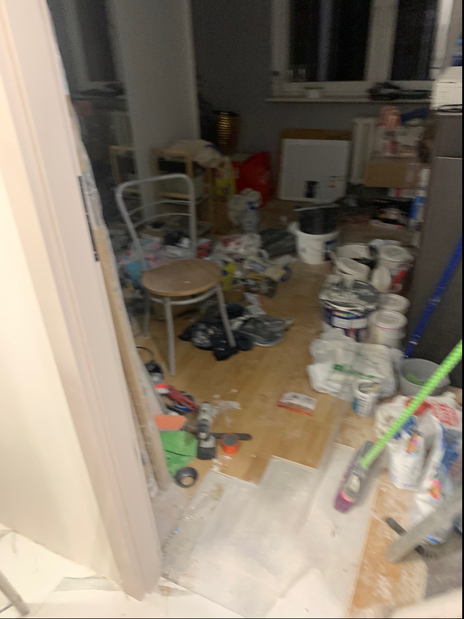 Remont pokoju w trakcie: widoczne narzędzia, puszki z farbą, częściowo ułożona podłoga i krzesło. Ujęcie z perspektywy wejścia do pomieszczenia, ukazujące etap prac wykończeniowych.