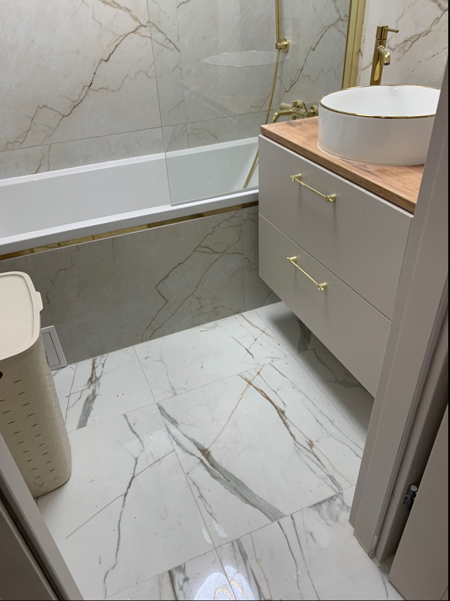 Elegancka łazienka z marmurowymi płytkami, złotymi akcentami i nowoczesną umywalką nablatową. Widoczna wanna i szafka z szufladami.