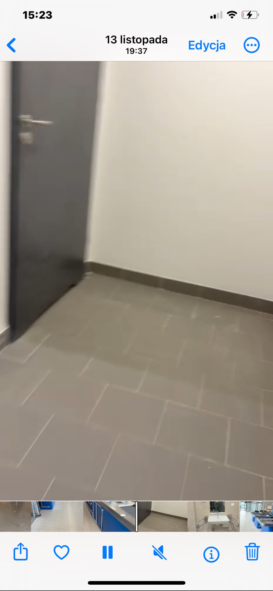 Wnętrze z szarymi płytkami podłogowymi i ciemnoszarą ścianą z drzwiami. Widok na fragment pomieszczenia z perspektywy podłogi, z widocznymi elementami wykończenia.