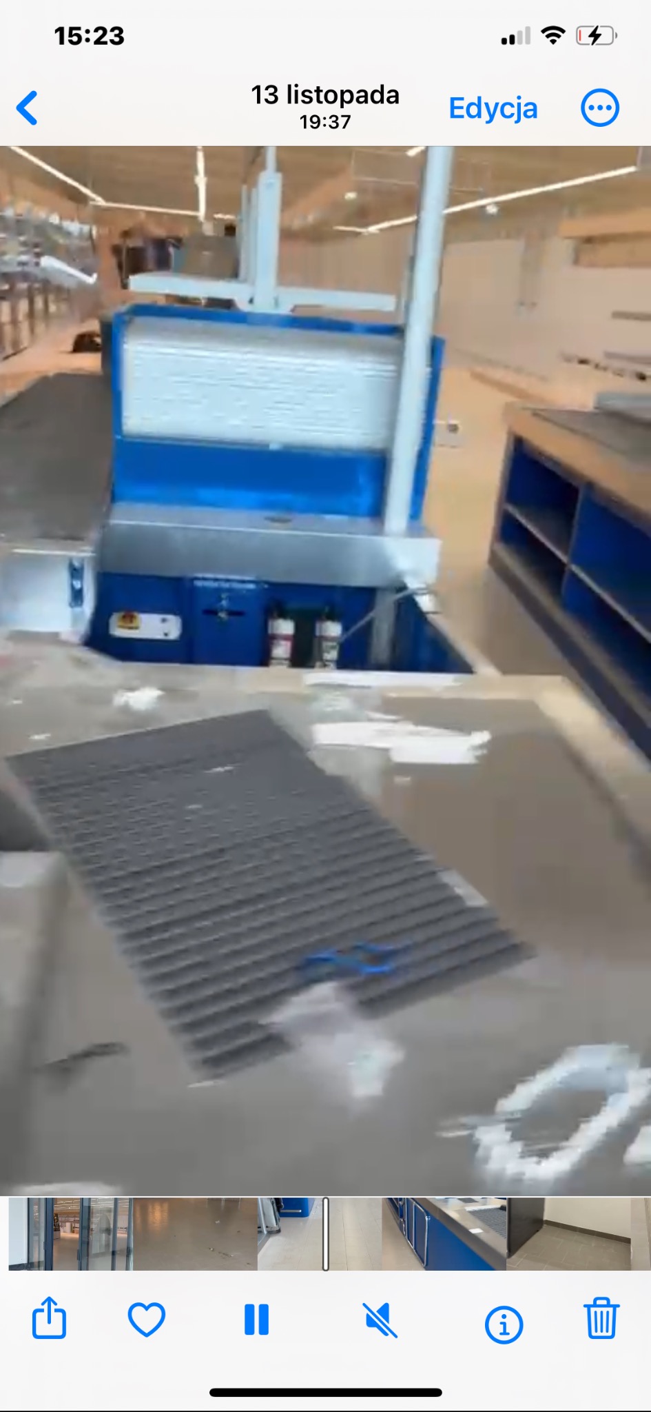 Wnętrze sklepu w trakcie sprzątania. Widoczny fragment podłogi z kratką ściekową, niebieskie regały i elementy wyposażenia. Rozproszone światło.