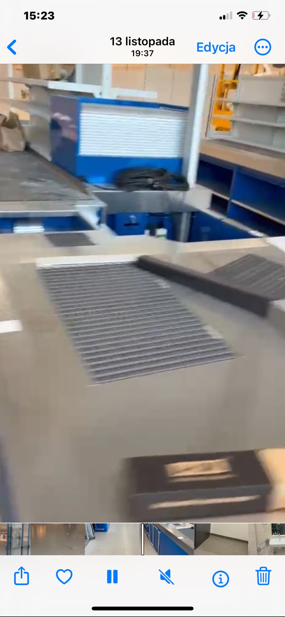 Metalowa krata wentylacyjna w podłodze, fragment niebieskiej konstrukcji i zwinięty kabel w tle. Widok z góry, oświetlenie naturalne.