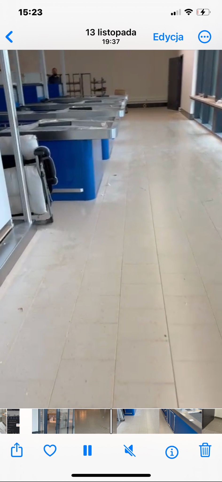 Wnętrze komercyjne z rzędem niebieskich stanowisk roboczych z metalowymi blatami, widok na czystą, jasną podłogę i odległą postać w tle. Perspektywa z dołu.