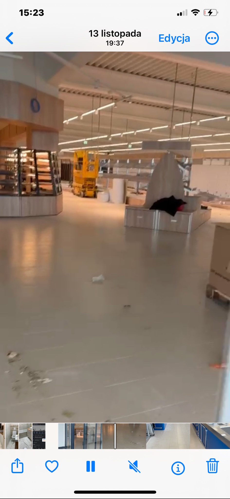 Wnętrze sklepu w trakcie remontu: widoczna podłoga, regały, podnośnik i elementy wyposażenia. Prace wykończeniowe w dużej przestrzeni handlowej.