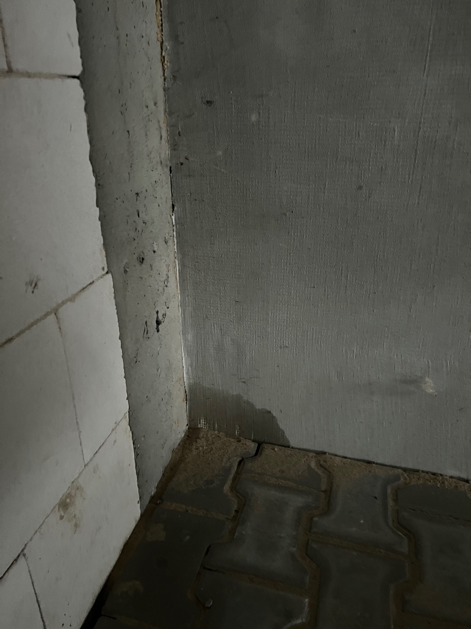 Szczegół narożnika w surowym stanie: białe bloczki, szara ściana z widocznymi śladami po pracach budowlanych i fragmentem szarej kostki brukowej na podłodze.