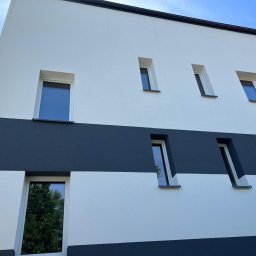 E-POWER ŁUKASZ CIERNIAK - Elewacja budynku po malowaniu w biało-grafitowe pasy, widok z dołu. Okna z wyraźnymi refleksami światła. Nowoczesny design.