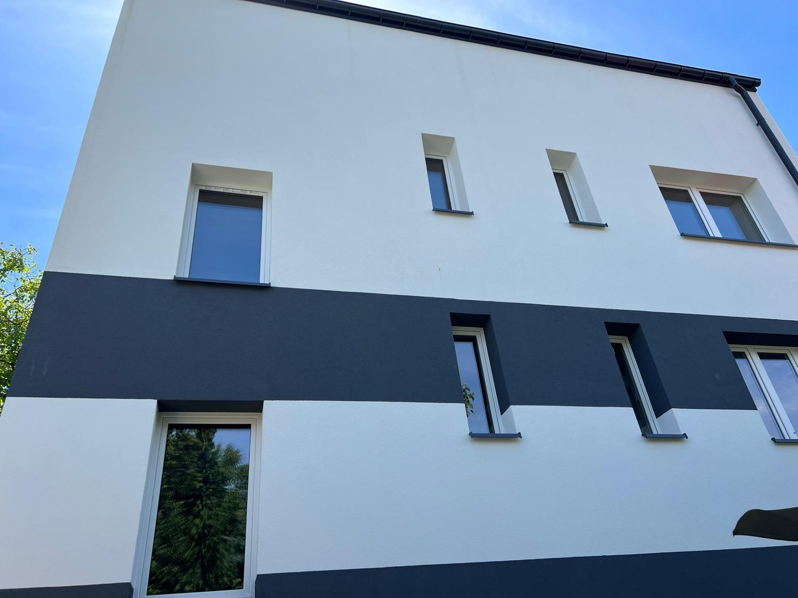 Elewacja budynku po malowaniu w biało-grafitowe pasy, widok z dołu. Okna z wyraźnymi refleksami światła. Nowoczesny design.