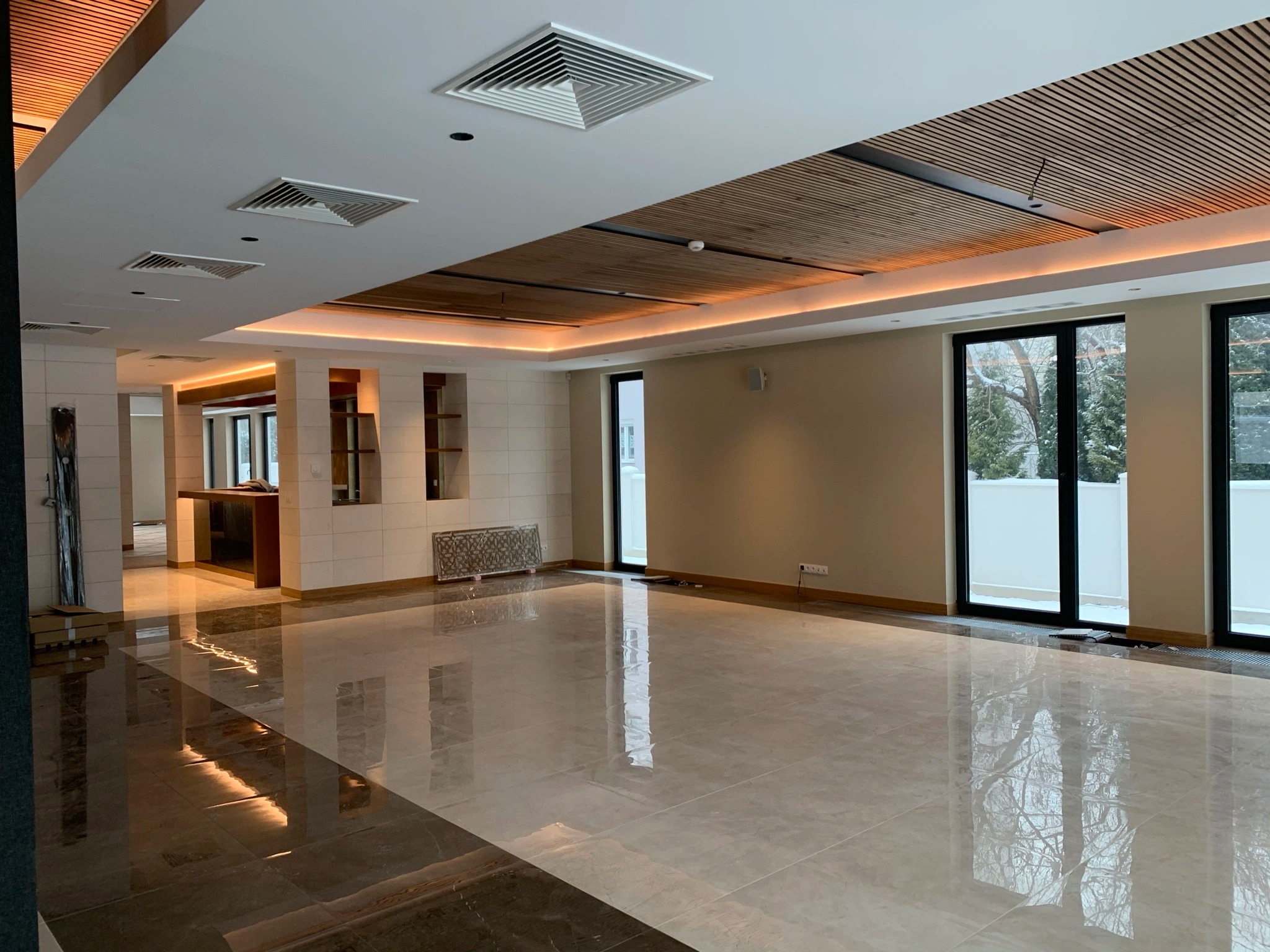 Przestronne wnętrze z błyszczącą podłogą, drewnianym sufitem z oświetleniem LED i dużymi oknami. Widoczny fragment baru i dekoracyjny grzejnik.