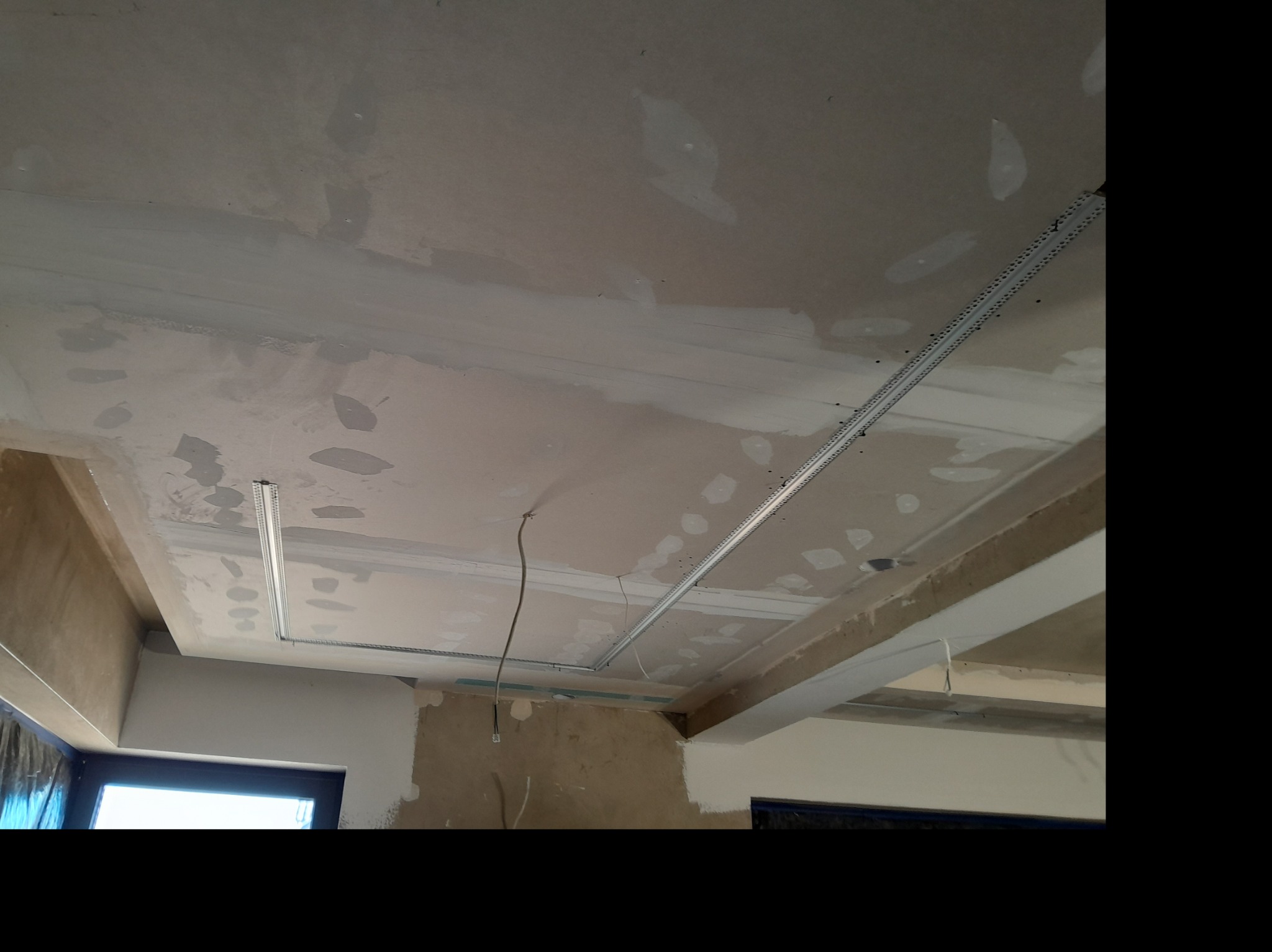 Sufit podwieszany w trakcie montażu: widoczne profile metalowe i częściowo położona płyta gipsowa, ślady szpachlowania. Przewody elektryczne wystają ze stropu.
