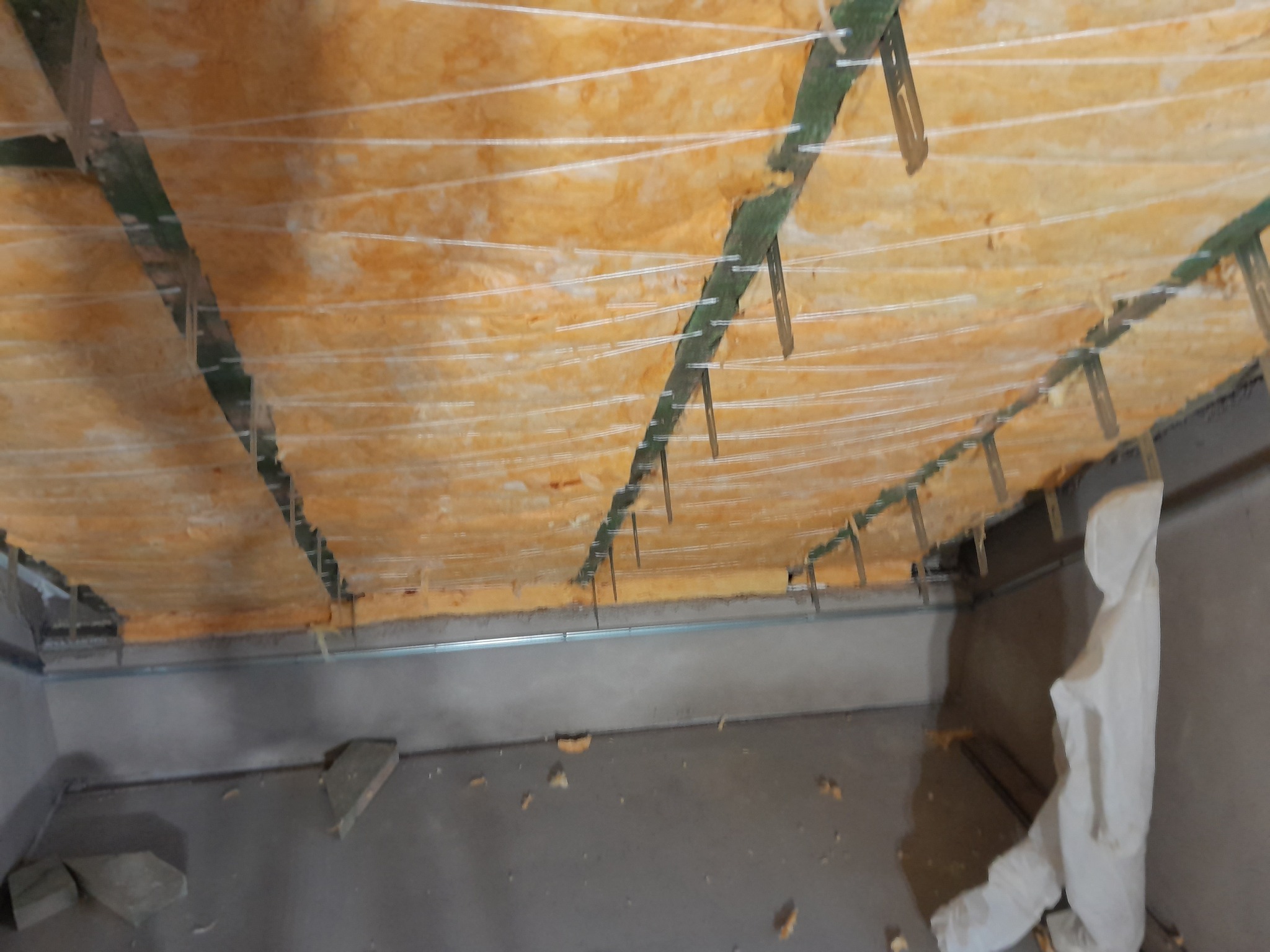 Ocieplenie poddasza wełną mineralną, widoczne metalowe profile i sznurki mocujące w Strzepczu. Prace wykończeniowe w trakcie realizacji, sufit w trakcie izolacji.