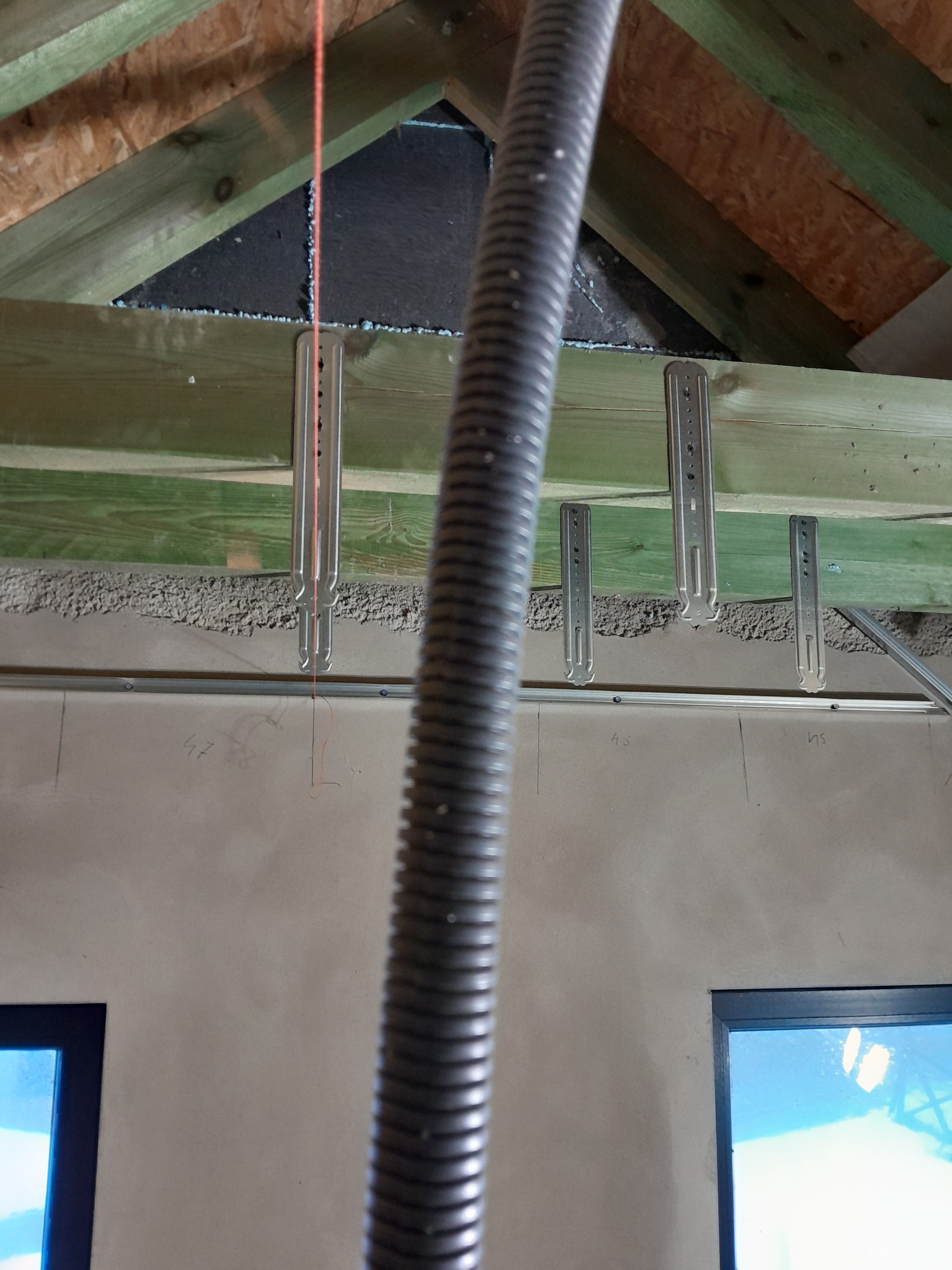 Montaż profili do płyt gipsowych na drewnianej konstrukcji dachu. Widoczna instalacja elektryczna w peszlu i fragment okna. Prace wykończeniowe na poddaszu.