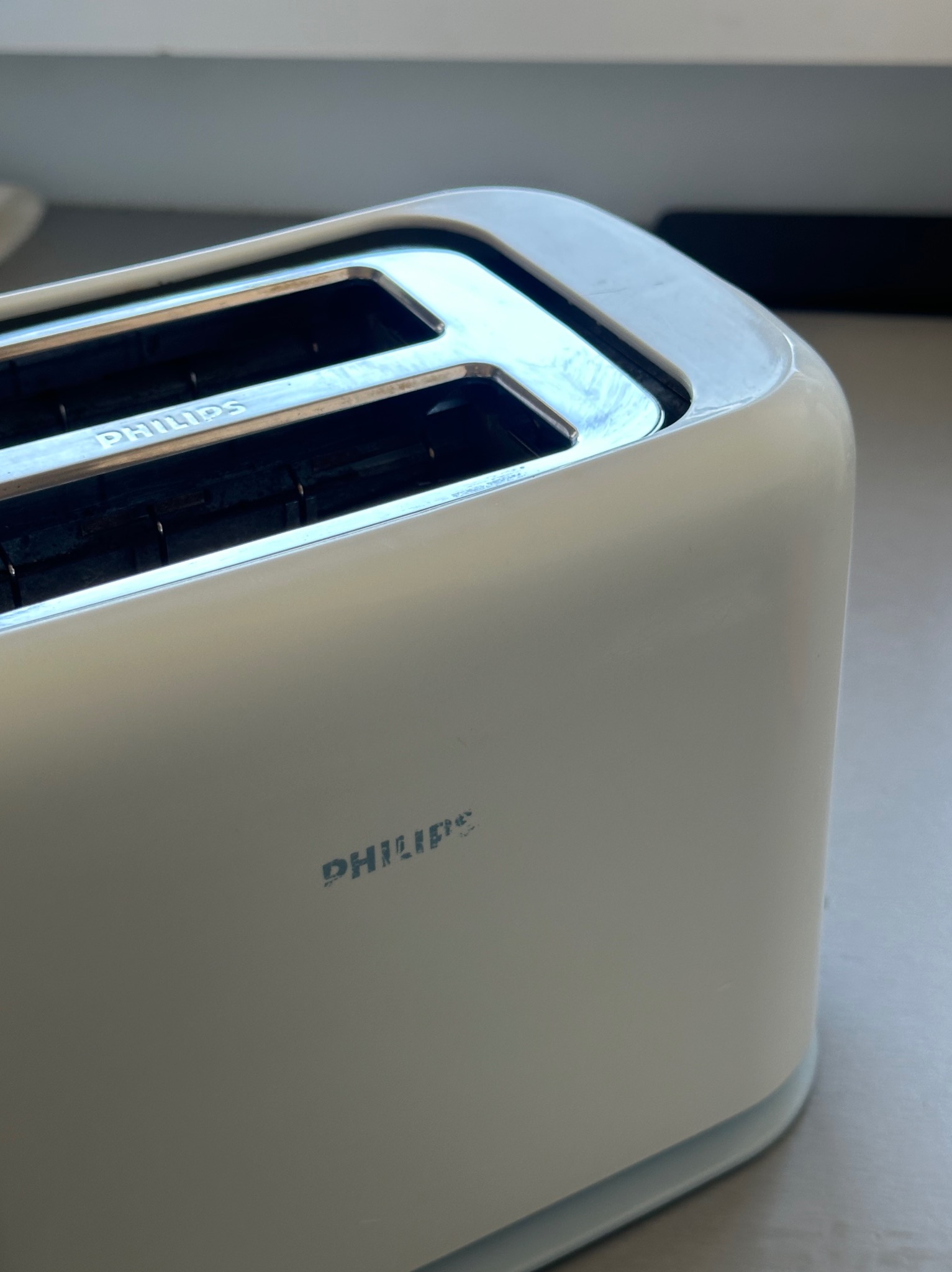 Biały toster Philips z dwoma szczelinami, ustawiony na blacie. Widoczny fragment blatu i ściany. Minimalistyczny design, czyste linie, delikatne światło.