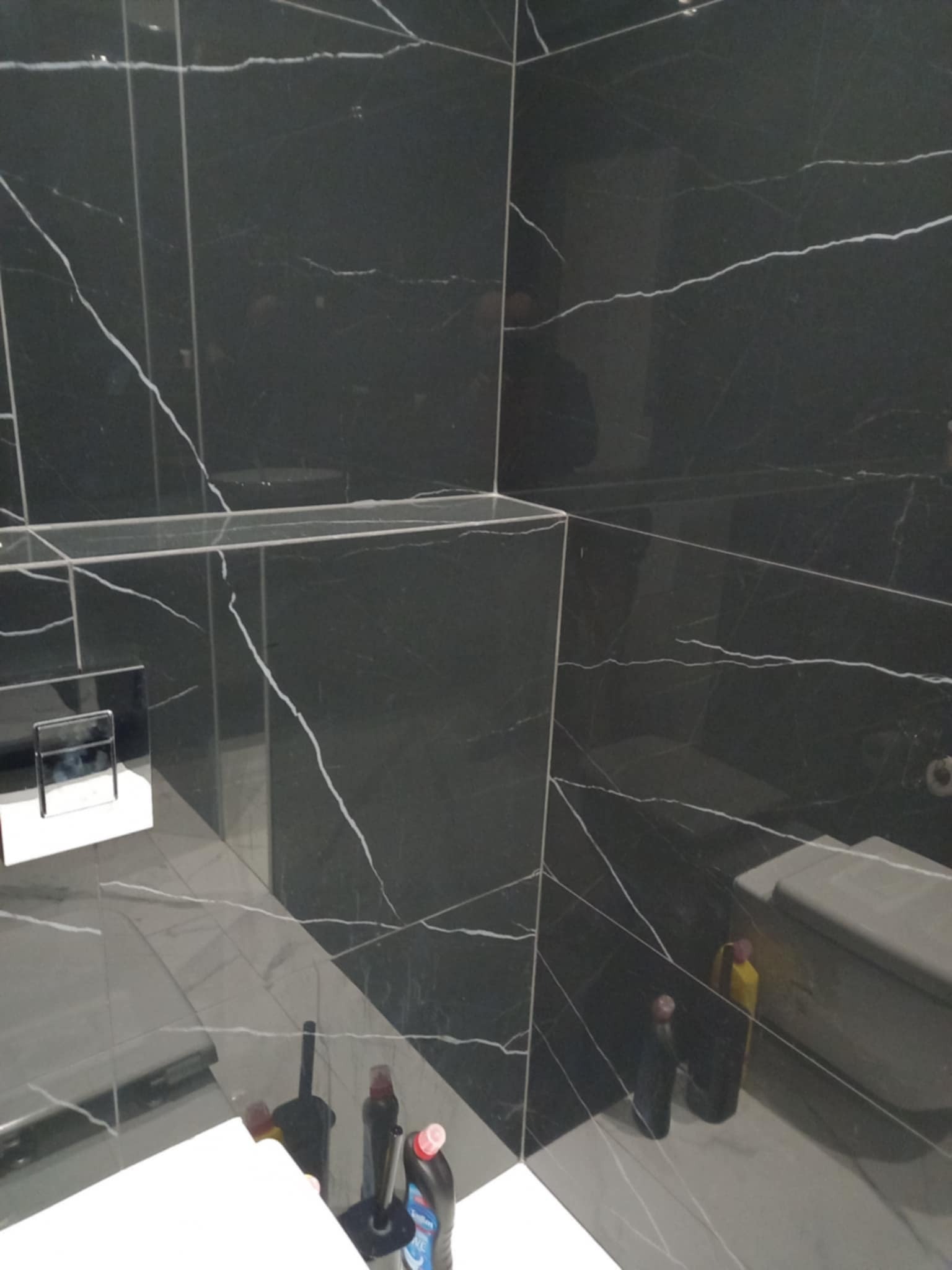 Elegancka łazienka wykończona czarnym marmurem z białymi żyłami. Widoczna armatura i akcesoria łazienkowe. Minimalistyczny design i nowoczesne wykończenie.