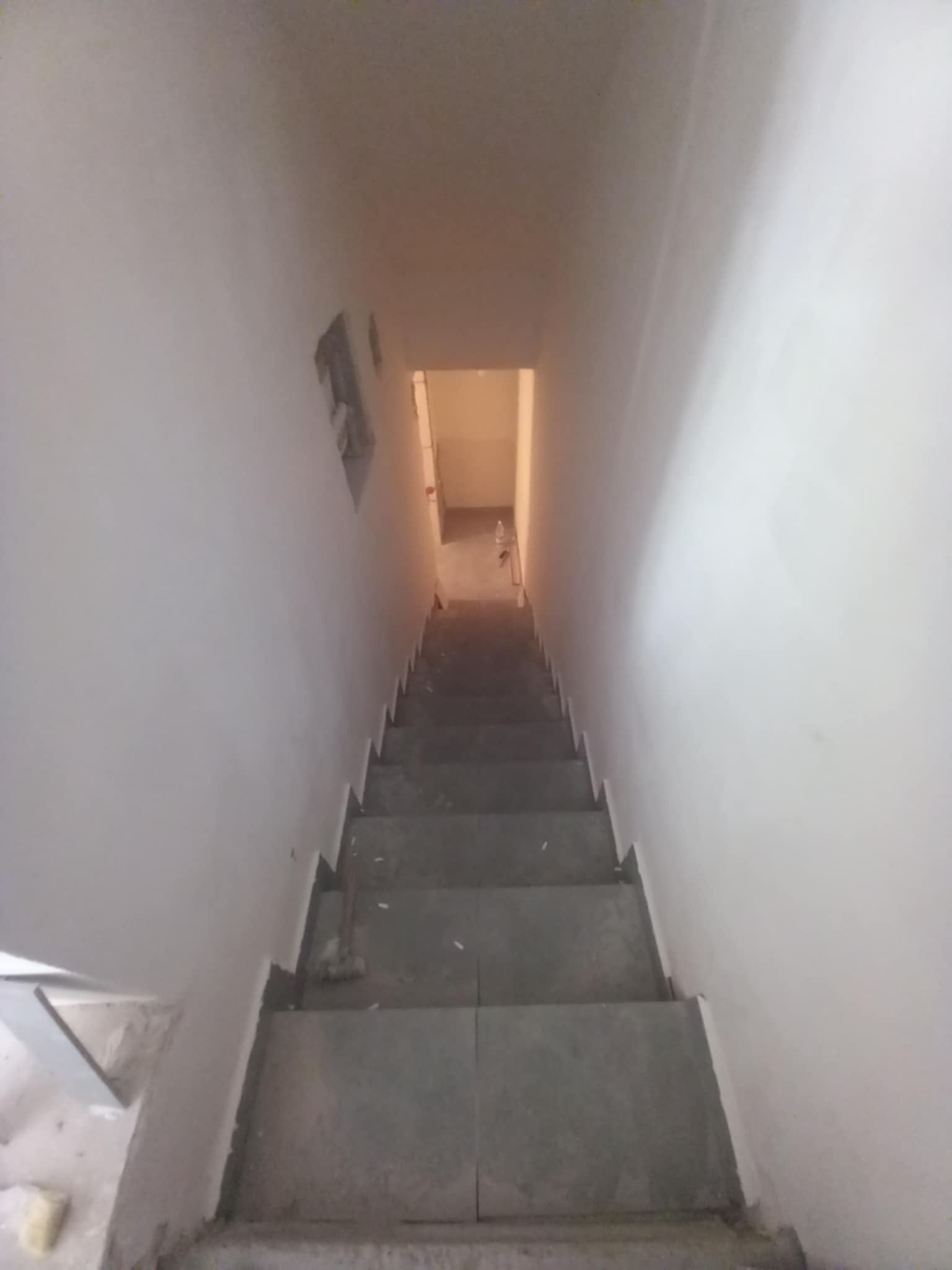 Schody w trakcie remontu: surowe ściany, szare stopnie, widoczne niedoskonałości i brak wykończenia. Ujęcie z góry podkreśla perspektywę i głębię przestrzeni.