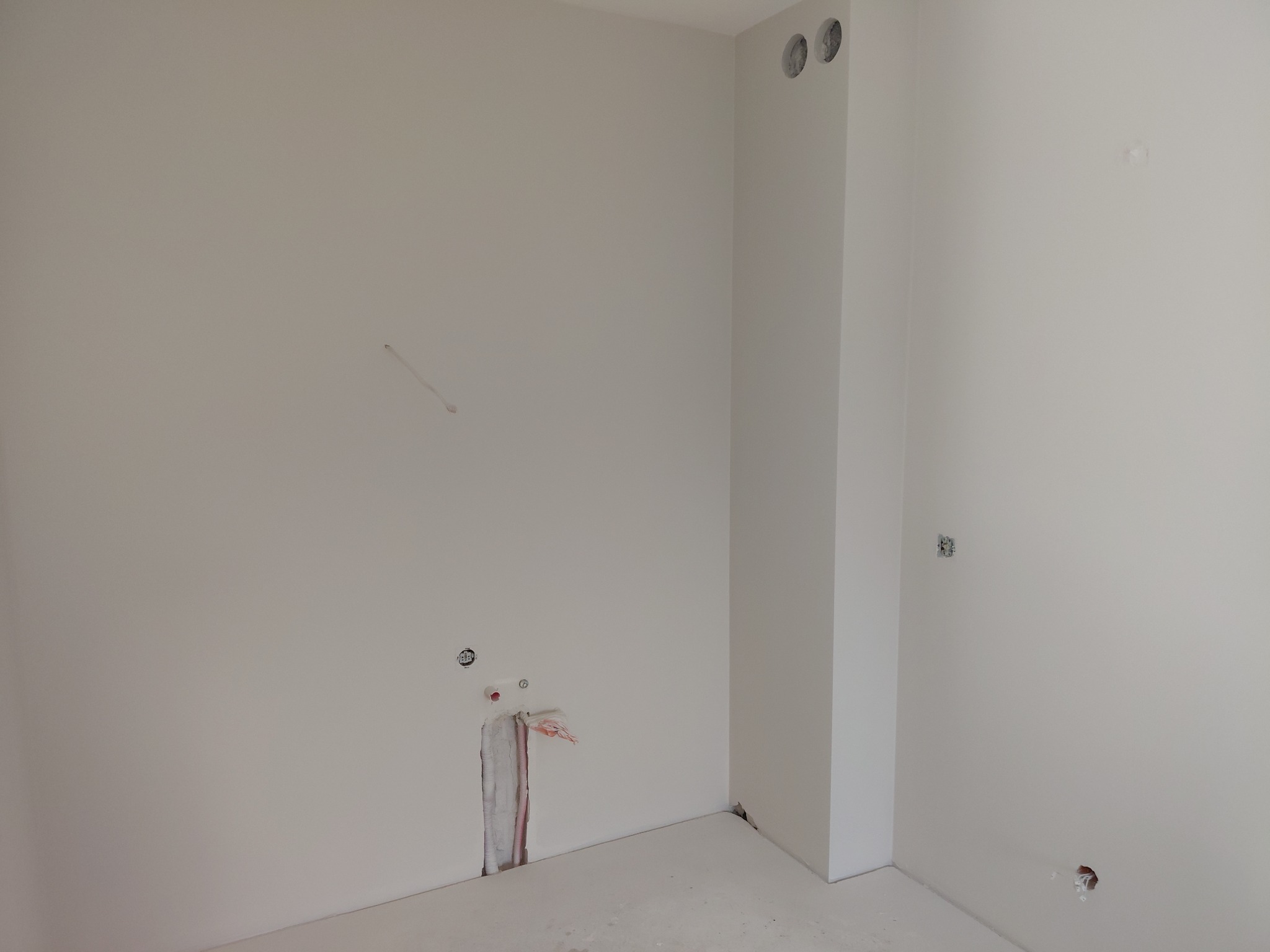 Wnętrze w trakcie prac wykończeniowych: gładkie, białe ściany, widoczne instalacje elektryczne i hydrauliczne w ścianach, przygotowane do dalszych prac.