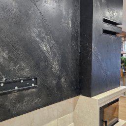 PM-Dekor Paweł Miklas - Eleganckie wykończenie ściany z efektem kamienia w odcieniach szarości, z wkomponowanym kominkiem i elementami z jasnego marmuru. Nowoczesny design wnętrza.