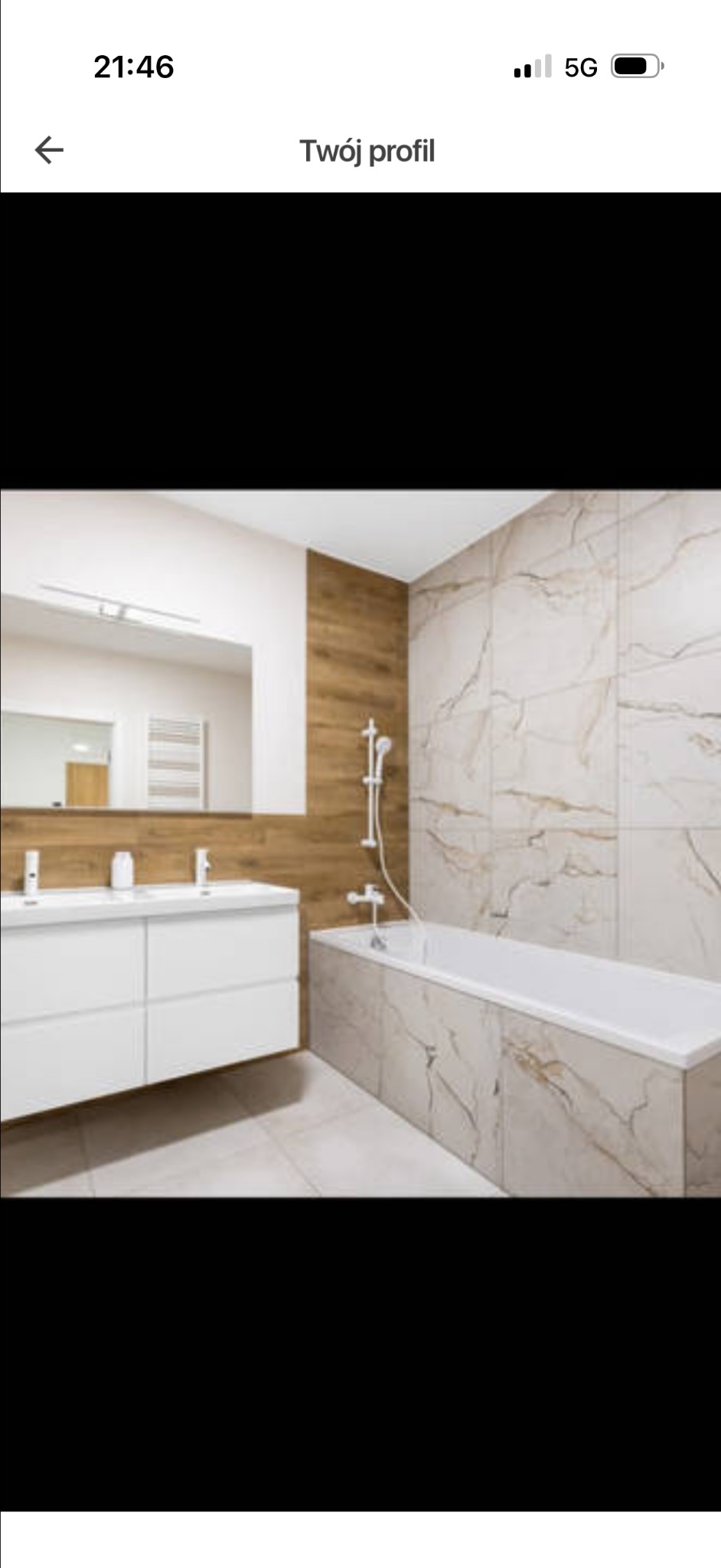 Nowoczesna łazienka z wanną obudowaną marmurowymi płytkami i białą szafką pod umywalką. Drewnopodobne panele na ścianie dodają ciepła wnętrzu.