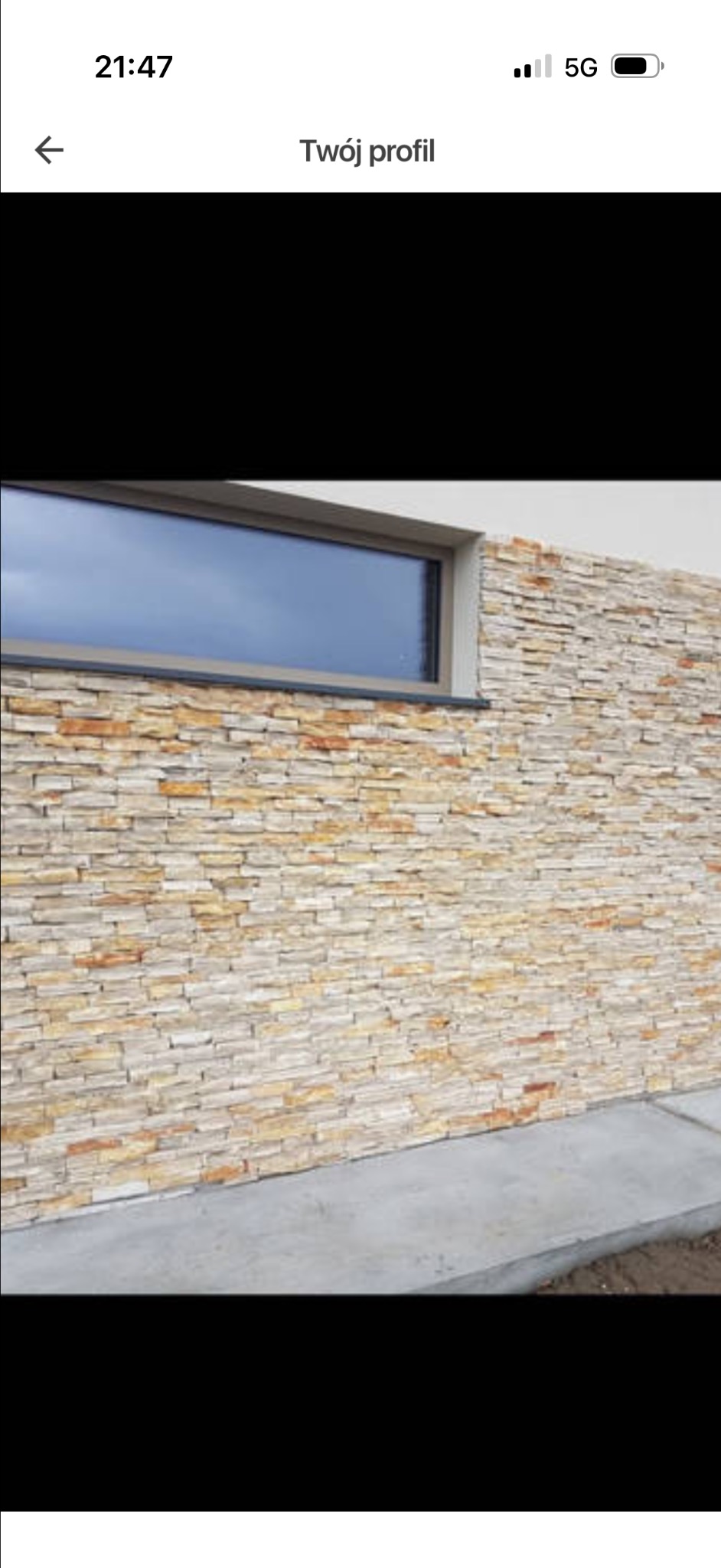 Elewacja budynku z dekoracyjnym kamieniem w odcieniach beżu i brązu, widoczna podłużna rama okienna. Nowoczesne wykończenie zewnętrzne.