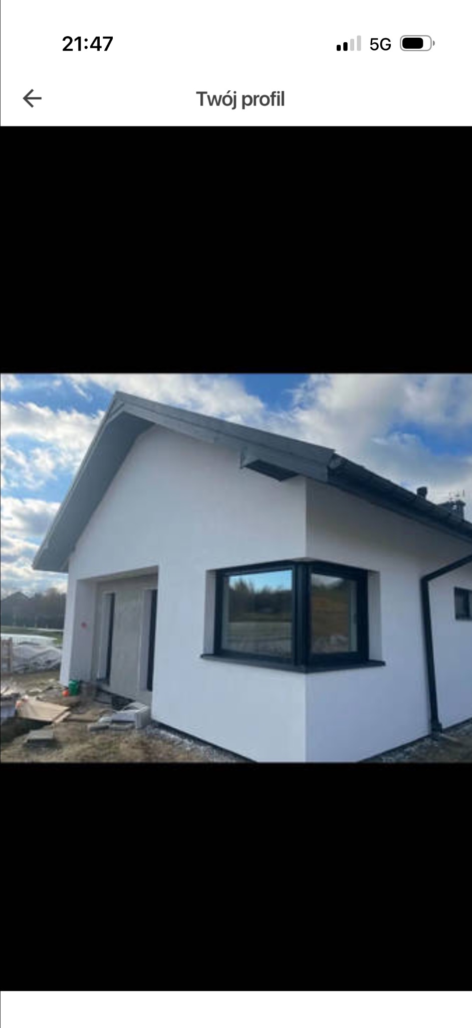 Biały dom jednorodzinny z czarną stolarką okienną i dachem, widoczny z zewnątrz, w trakcie prac wykończeniowych. Okno narożne z refleksami krajobrazu.