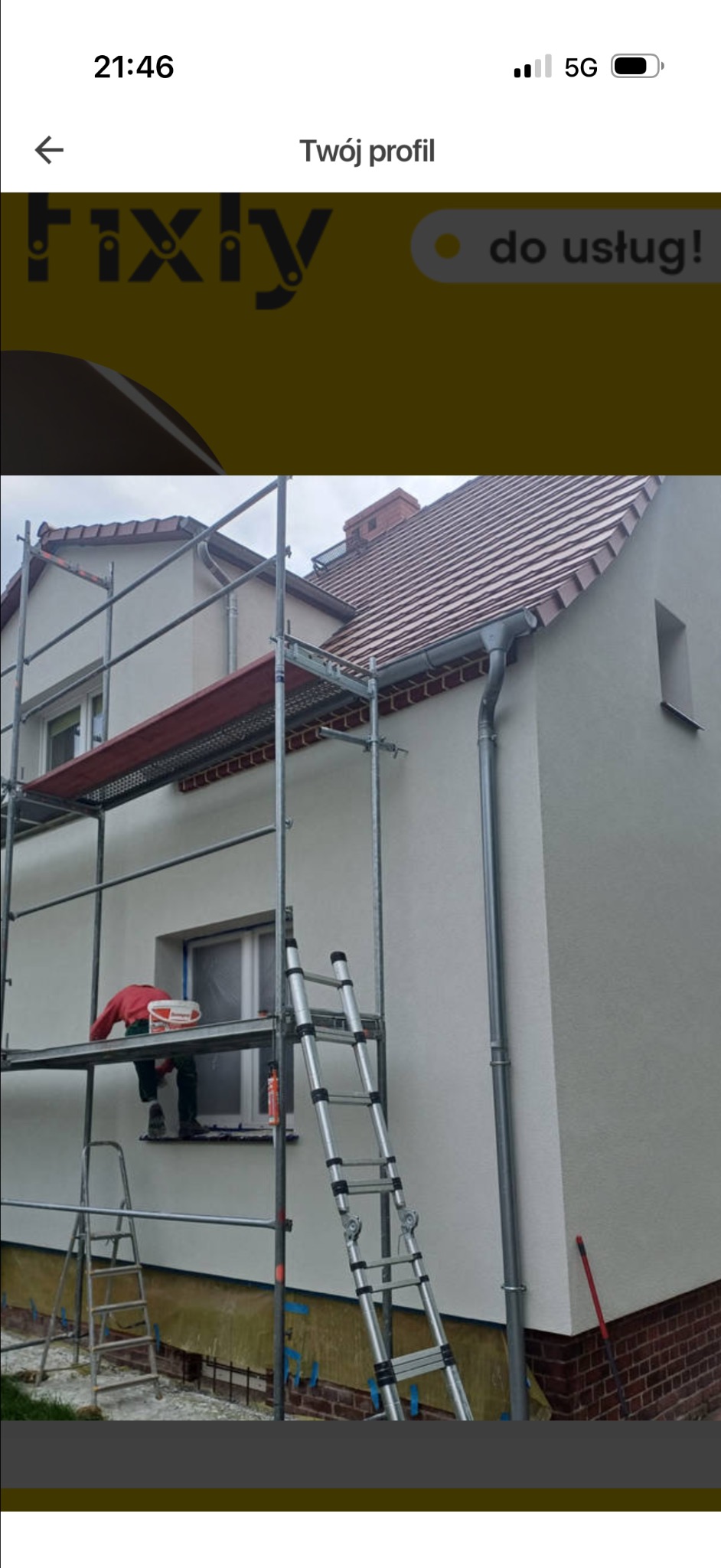 Ocieplanie elewacji domu jednorodzinnego. Pracownik na rusztowaniu, widoczne narzędzia i materiały budowlane. Świeżo otynkowana ściana, nowy system rynnowy.