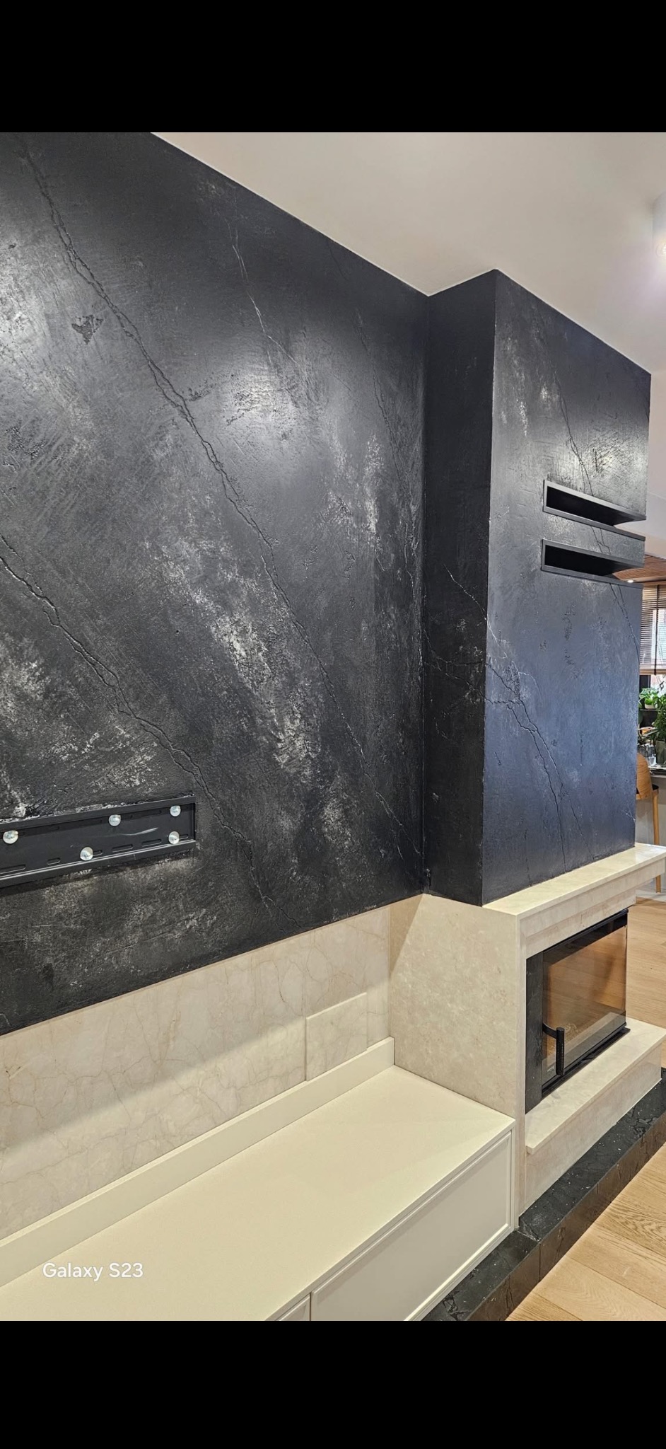 Eleganckie wykończenie ściany z efektem kamienia w odcieniach szarości, z wkomponowanym kominkiem i elementami z jasnego marmuru. Nowoczesny design wnętrza.