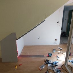 Wykończenia Fot-mar S.A. - Adaptacja poddasza: montaż płyty G-K na skosach, widoczne profile, narzędzia i laser krzyżowy. Prace wykończeniowe w trakcie, surowe ściany, przygotowanie do zabudowy.