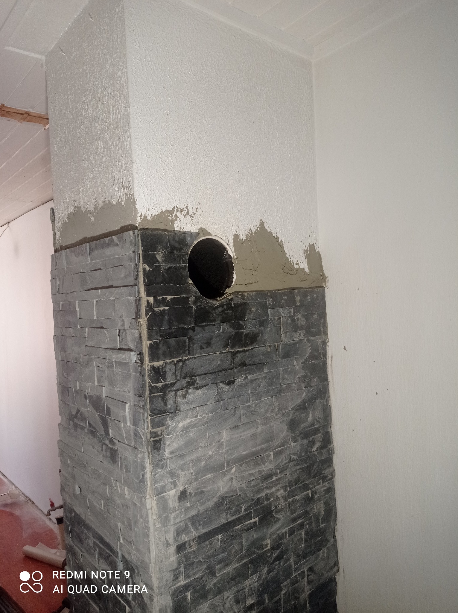 Fragment ściany z dekoracyjną okładziną imitującą kamień, z widocznym otworem i śladami świeżego szpachlowania na górze. Prace wykończeniowe w trakcie.