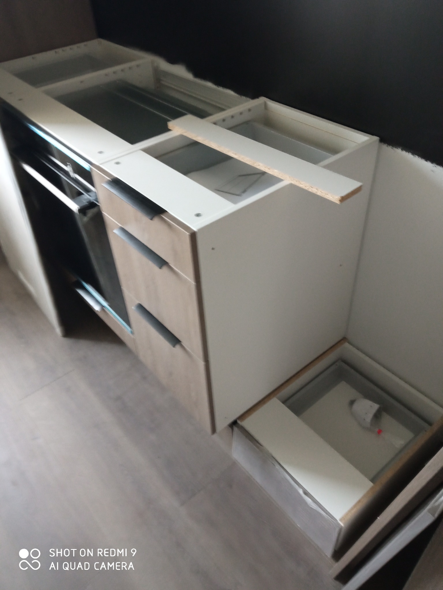 Fragment montażu szafek kuchennych z szufladami i piekarnikiem, widoczne elementy konstrukcyjne i niedokończone wykończenie, wnętrze w trakcie realizacji.