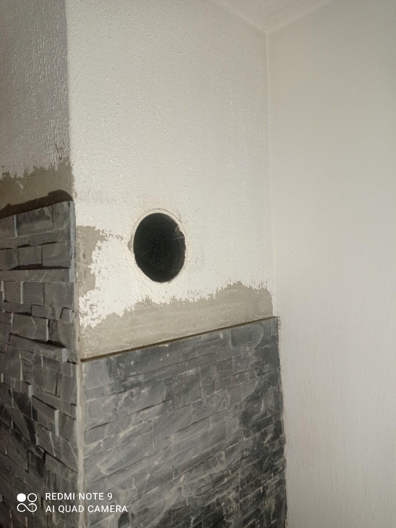 Fragment ściany z otworem i częściowo położoną dekoracyjną okładziną kamienną. Widoczne ślady zaprawy i świeżo pomalowana ściana. Ujęcie z dołu.