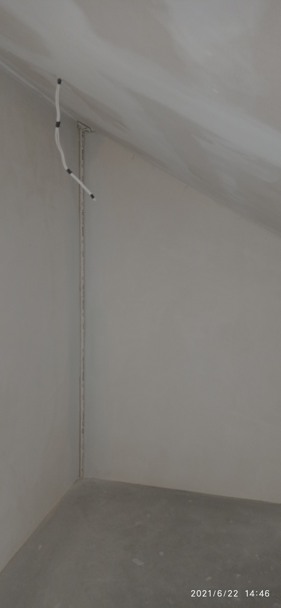 Szpachlowana ściana pod skosem z wystającymi przewodami elektrycznymi i listwą przypodłogową. Przygotowanie do malowania w jasnym pomieszczeniu.