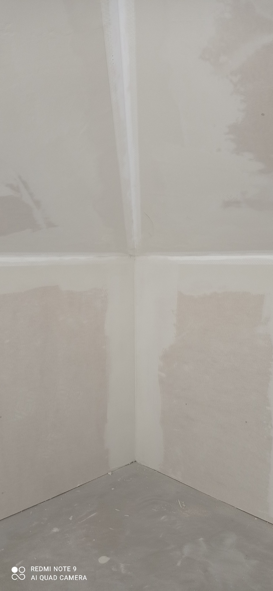 Wnętrze w trakcie prac wykończeniowych: ściany i sufit pokryte szpachlą, widoczne łączenia płyt gipsowo-kartonowych. Przygotowanie do malowania.