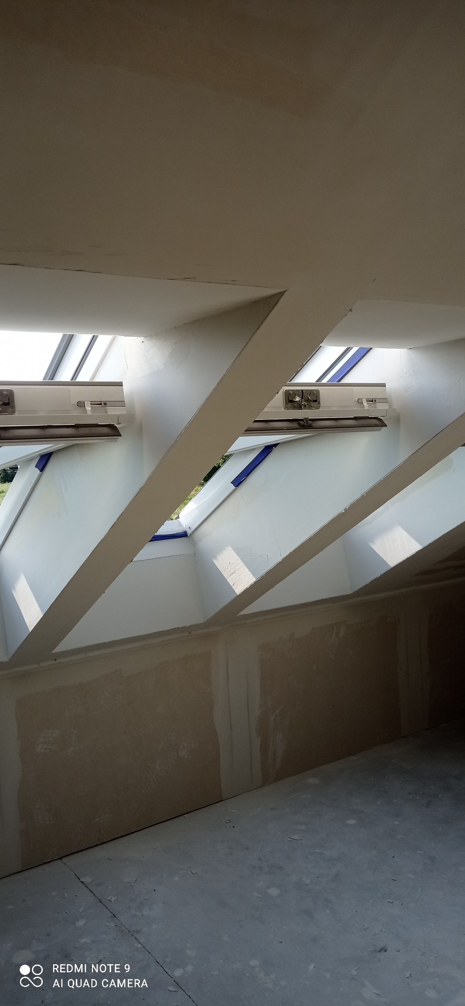 Poddasze z oknami dachowymi po szpachlowaniu, widoczne łączenia płyt gipsowo-kartonowych przygotowane do malowania. Ujęcie z dołu, surowe wykończenie.