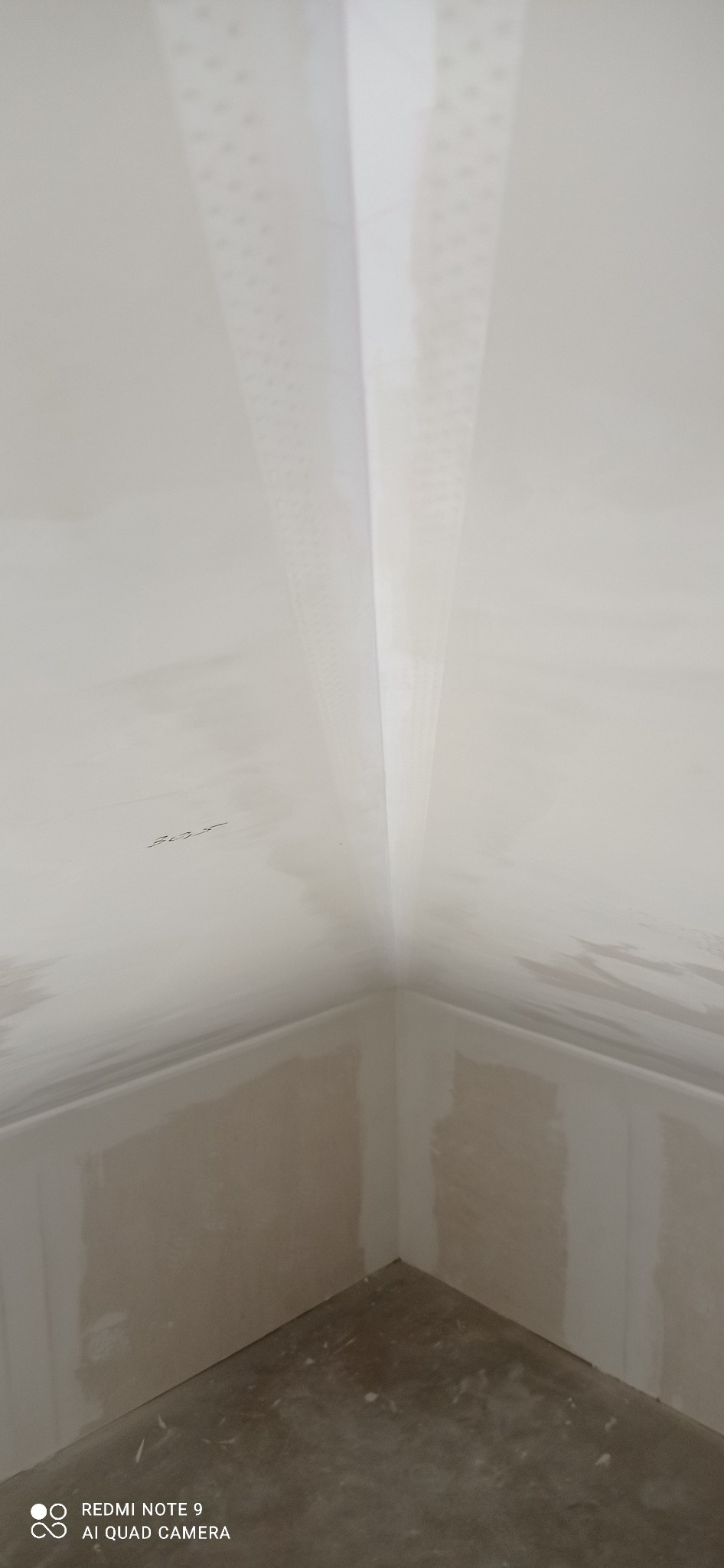 Wnętrze w trakcie prac wykończeniowych: połączenie ściany i sufitu z widoczną siatką wzmacniającą na suficie. Ściany przygotowane do malowania, surowy beton na podłodze.