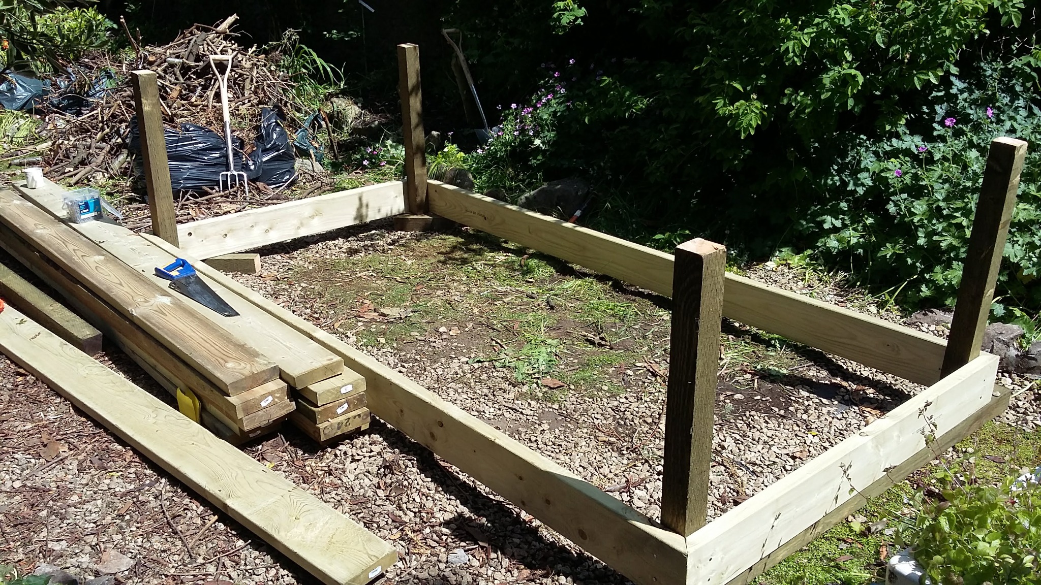 Drewniana konstrukcja szkieletowa, prawdopodobnie pod podest lub taras, w trakcie budowy. Widoczne deski, słupki, narzędzia i otoczenie zieleni.