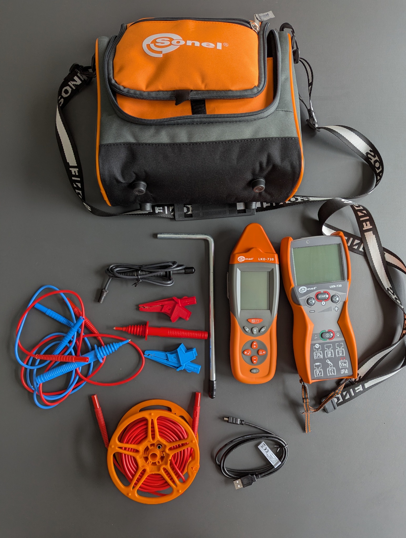 Zestaw narzędzi pomiarowych Sonel: mierniki LKO-720 i LKN-720, przewody, torba transportowa. Sprzęt do pomiarów elektrycznych na szarym tle.