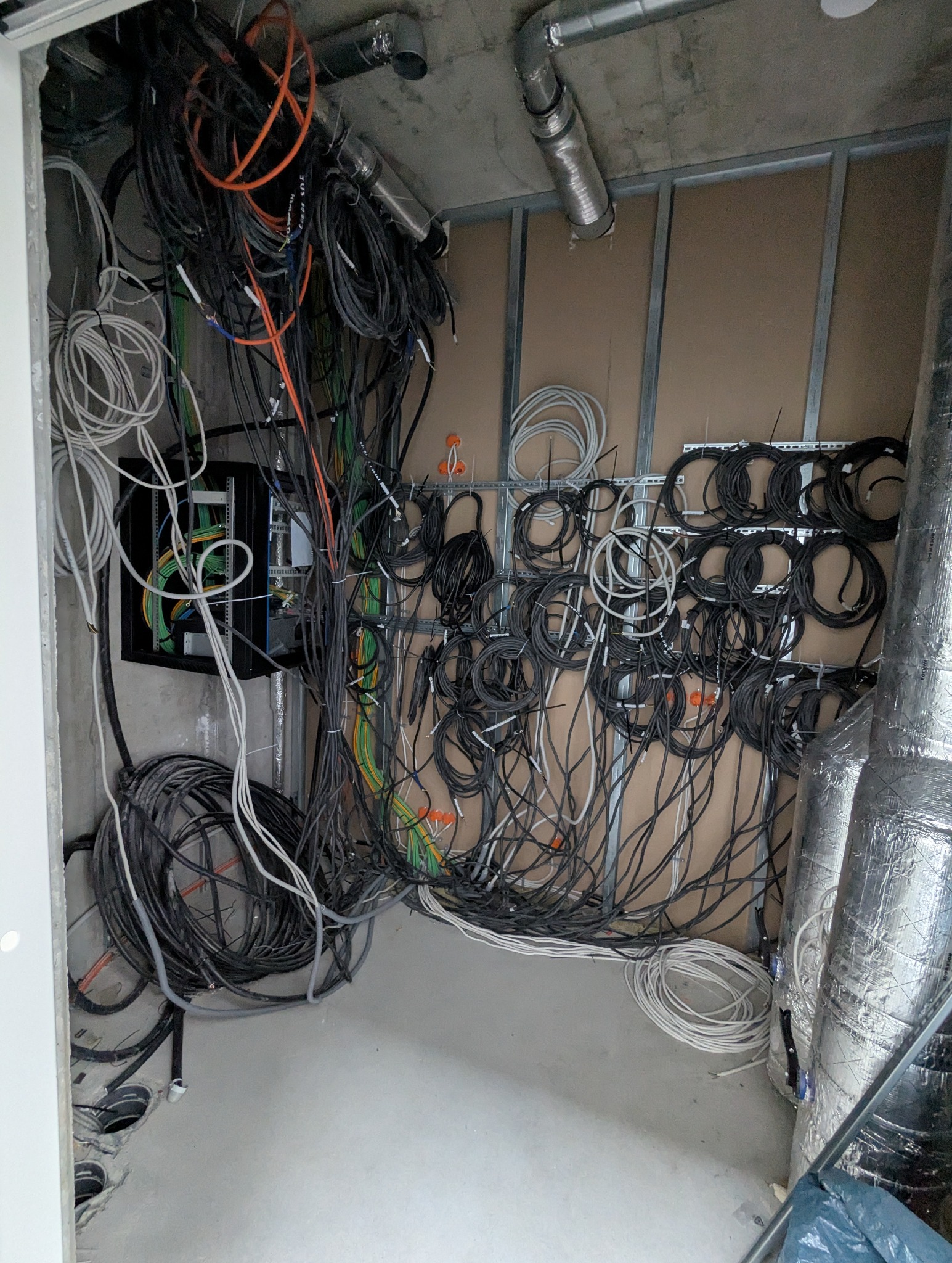 Skomplikowana sieć kabli elektrycznych i rur wentylacyjnych w surowym wnętrzu, widoczne elementy instalacji w trakcie montażu na ścianie z płyt kartonowo-gipsowych.