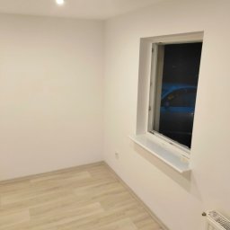 Paweł - Pomalowane na biało wnętrze pokoju z jasną podłogą, oknem z widokiem na noc i białym grzejnikiem. Minimalistyczny design, świeżo po remoncie.