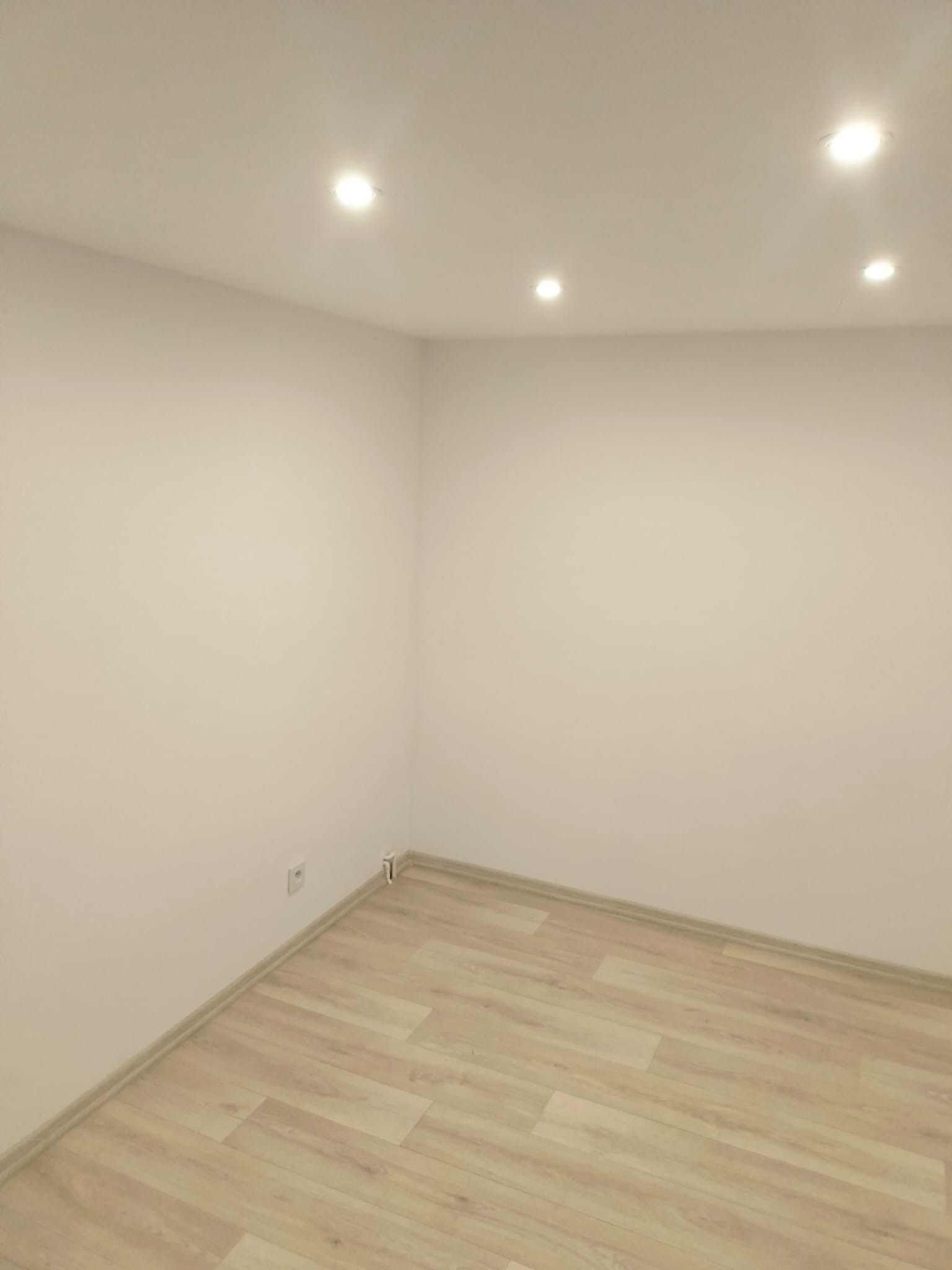 Jasne wnętrze pokoju po remoncie: świeżo pomalowane ściany w odcieniach bieli, panele podłogowe imitujące drewno, oświetlenie sufitowe punktowe. Minimalistyczny styl.