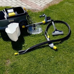 Usługi czyszczące Ziela - Profesjonalny odkurzacz piorący Karcher z akcesoriami na trawie w słoneczny dzień. Sprzęt do prania dywanów i tapicerki, widoczny zbiornik na wodę i różne końcówki.