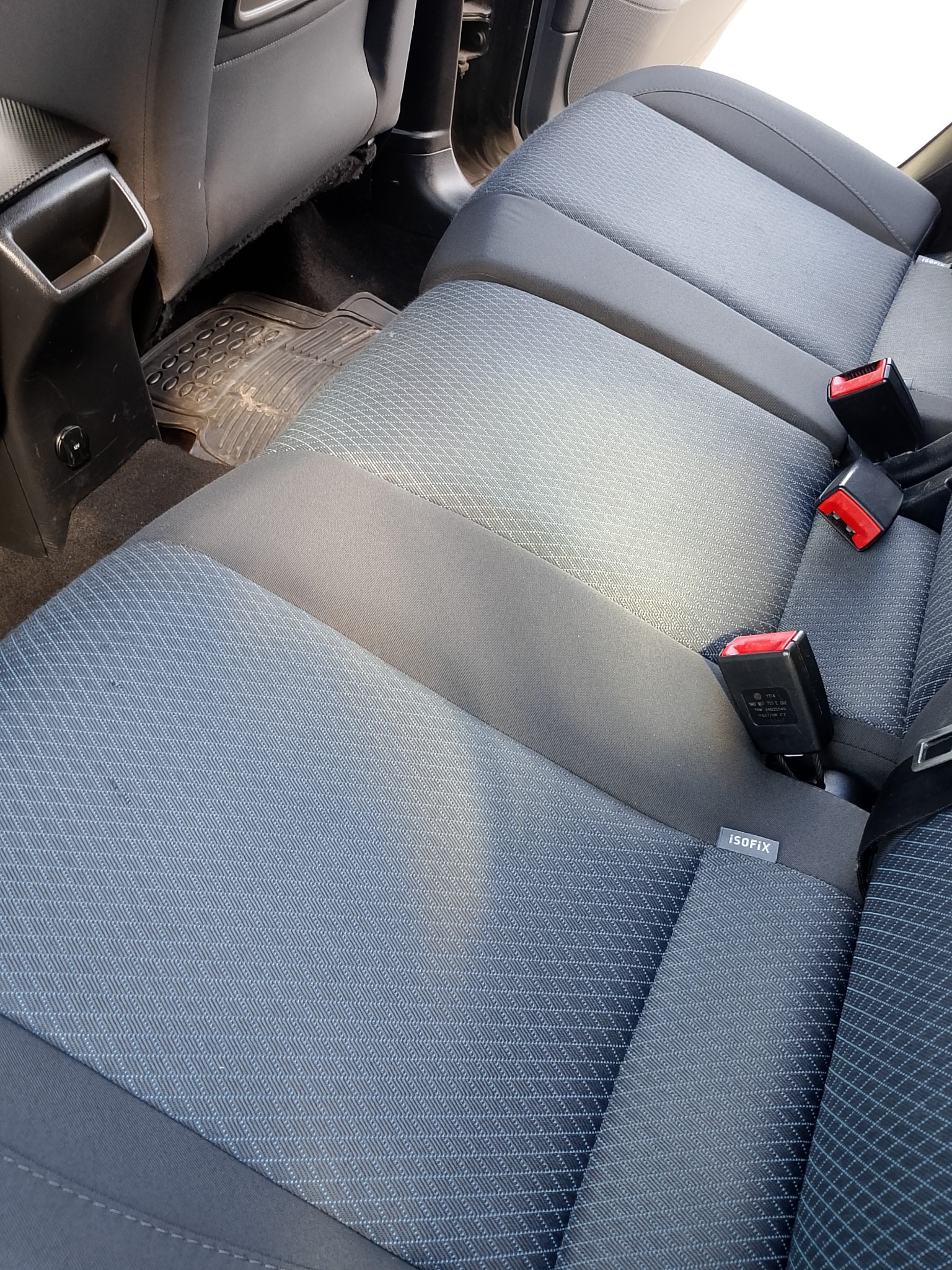 Szare, tekstylne siedzenie samochodowe z widocznymi pasami bezpieczeństwa i oznaczeniem ISOFIX. Widoczna gumowa wycieraczka pod siedzeniem.