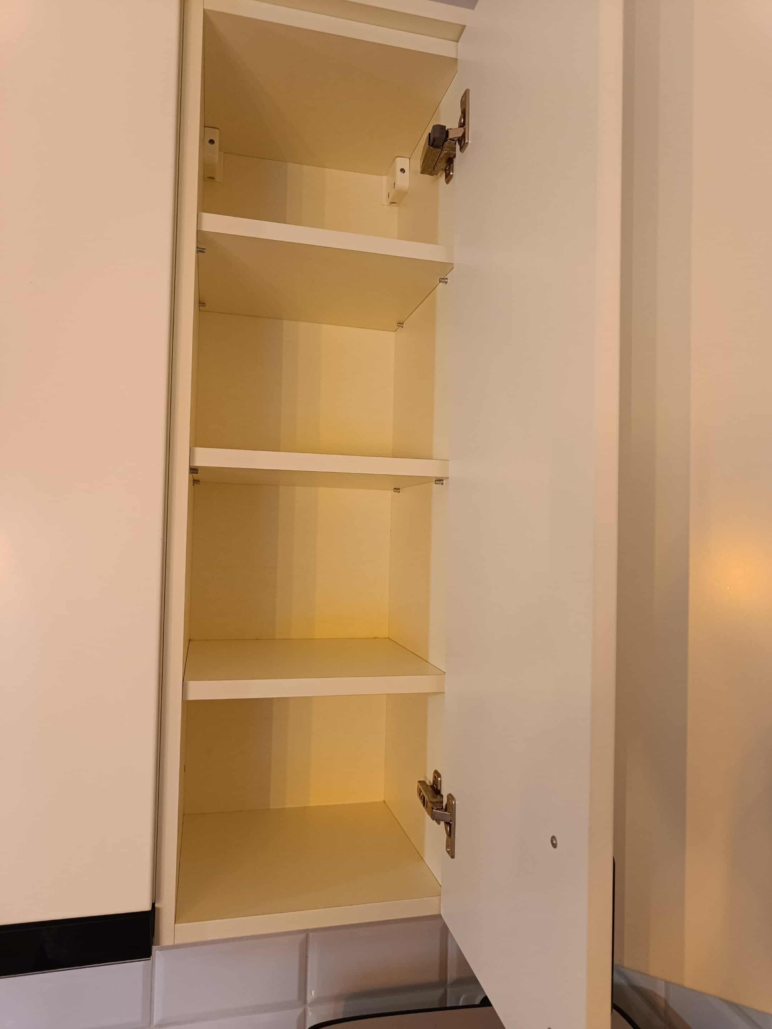 Otwarta, pusta szafka kuchenna z jasnymi półkami i widocznymi zawiasami, ukazująca wnętrze przedmiotu przed sprzątaniem lub po opróżnianiu.