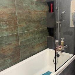 MNBwnetrza - Wykończona łazienka z wanną, szklanym parawanem i oryginalnymi płytkami w odcieniach brązu i zieleni. Wnęka w ścianie z kosmetykami. Nowoczesny design.