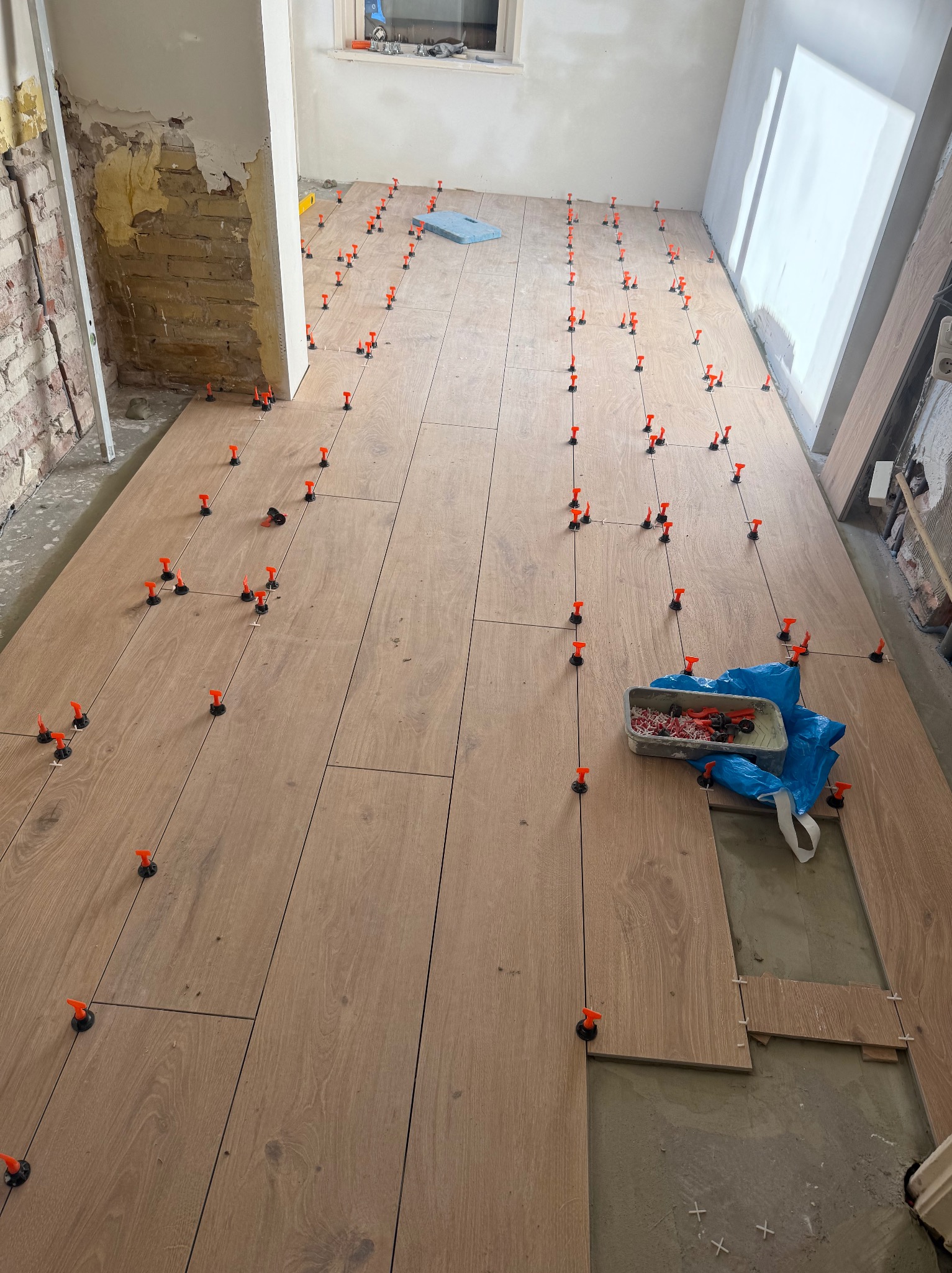 Układanie podłogi z paneli drewnopodobnych z użyciem klipsów poziomujących. Częściowo wykończone pomieszczenie w trakcie prac. Widoczne narzędzia i materiały.