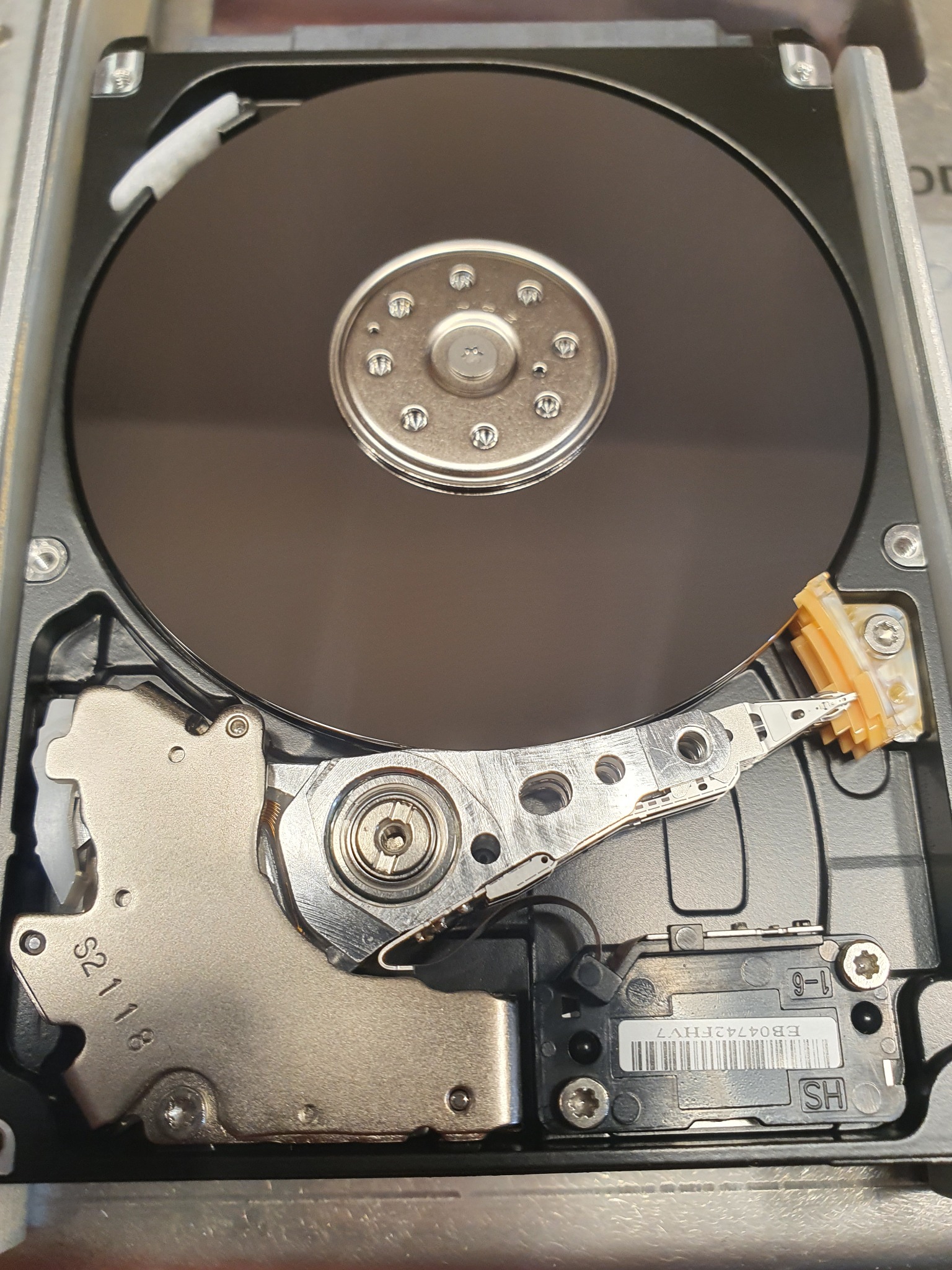 Otwarty dysk twardy z widoczną głowicą i talerzem, detale mechaniczne, numer seryjny EB04742FHV7, oznaczenie S2118. Precyzyjne ujęcie wnętrza nośnika danych.