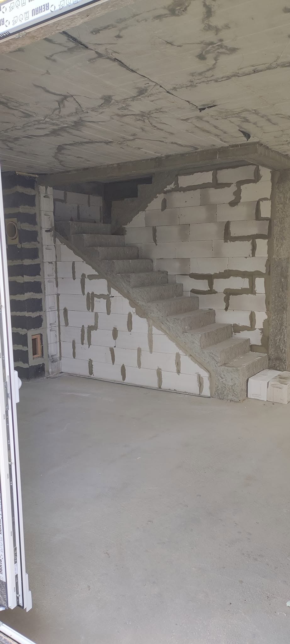 Wnętrze w trakcie budowy: surowy betonowy strop, ściany z białych bloczków, wznoszone schody z betonu, widoczne instalacje. Stan surowy zamknięty.