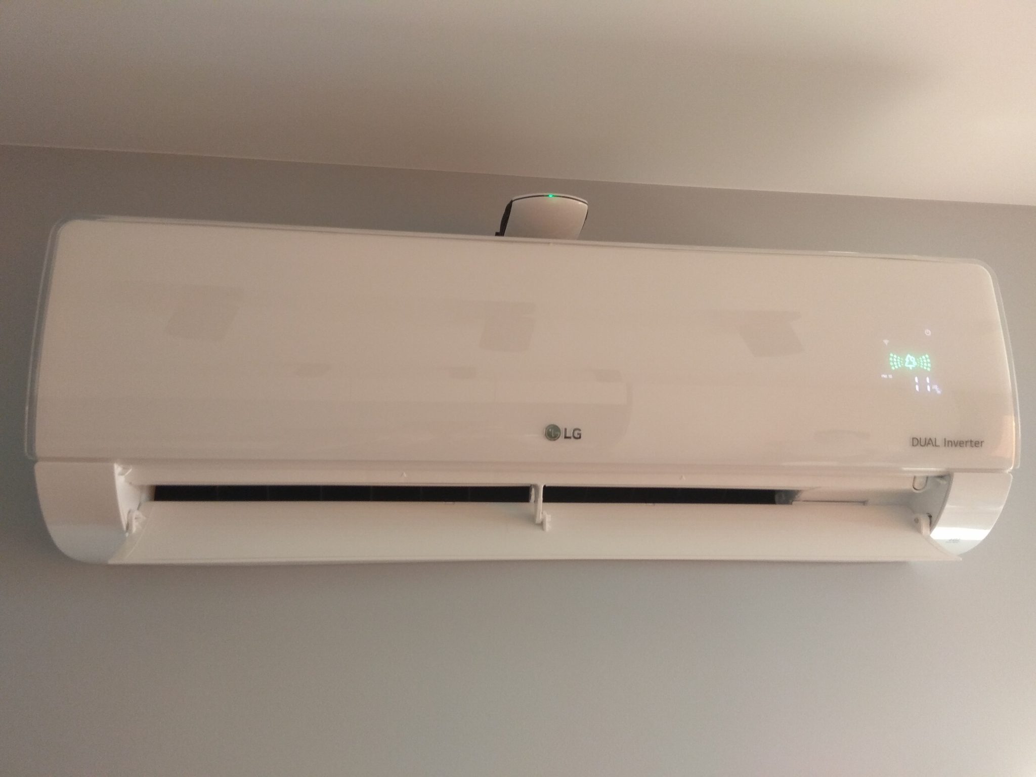 Biała klimatyzacja LG Dual Inverter zamontowana na szarej ścianie, widoczne diody sygnalizacyjne i czujnik. Minimalistyczny design, nowoczesne wnętrze.