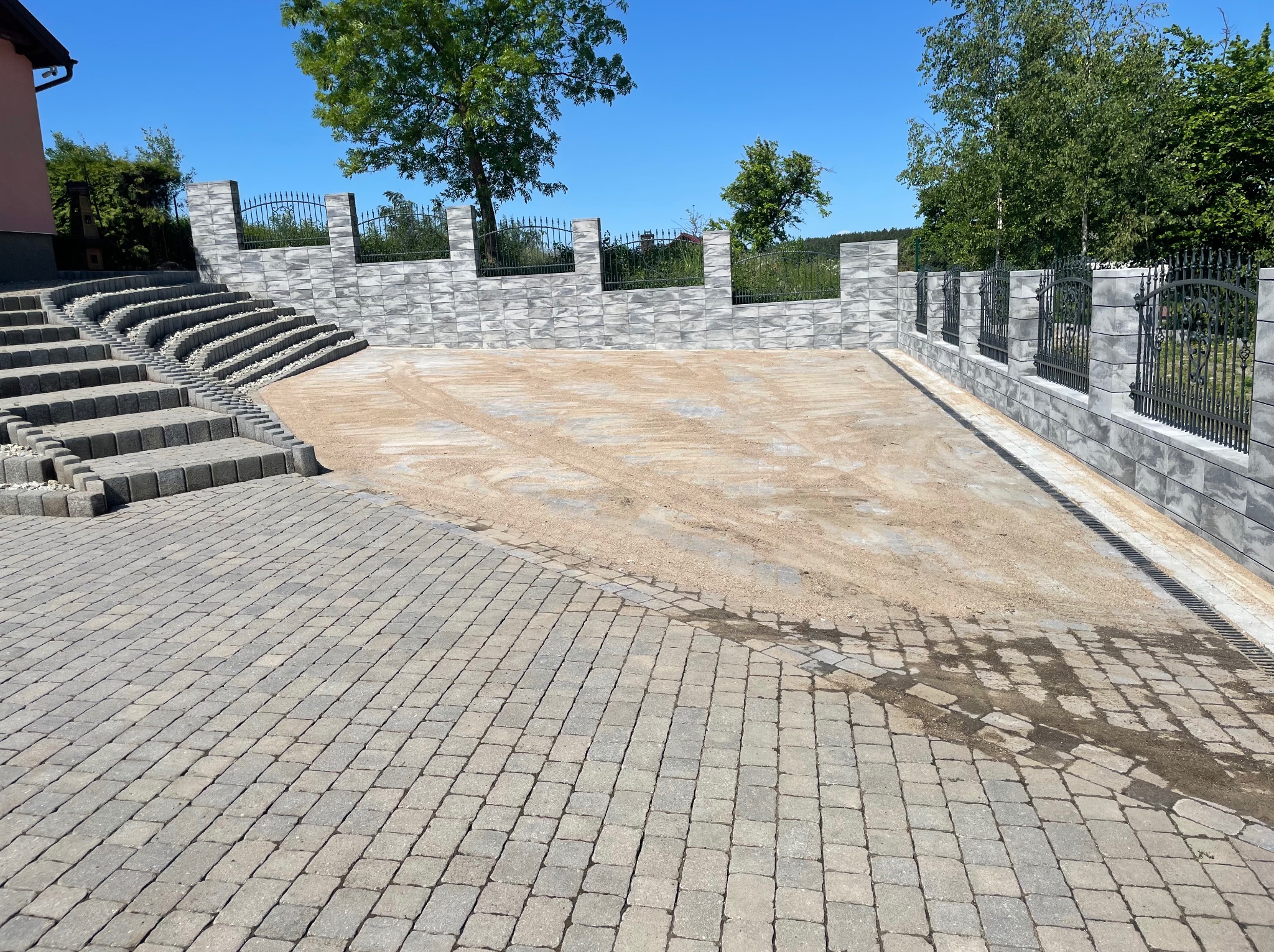 Ułożona kostka brukowa na podjeździe w Starogardzie Gdańskim, widoczne schody i ogrodzenie z szarej kostki. Przygotowany teren pod dalsze prace.