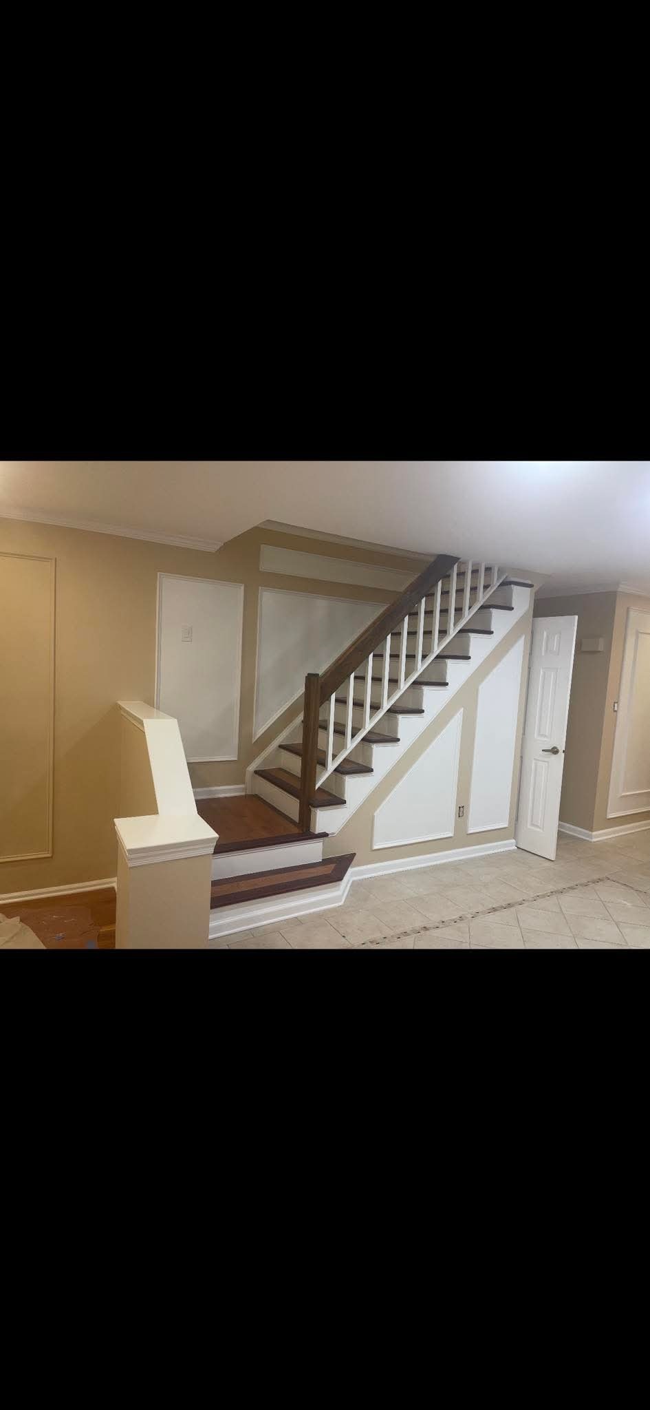 Odnowione schody z drewnianymi stopniami i białymi balustradami w jasnym wnętrzu. Ściany w odcieniach beżu z dekoracyjnymi panelami. Widoczna podłoga z płytek.